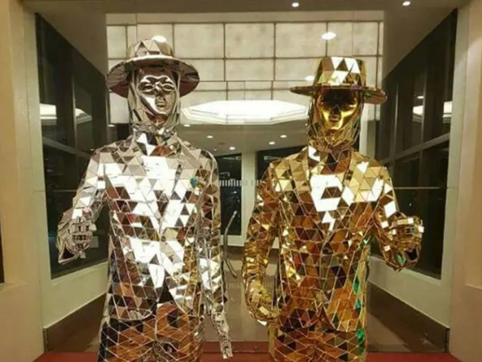 Silver mirror man and golden mirror man together at the entrance of an event