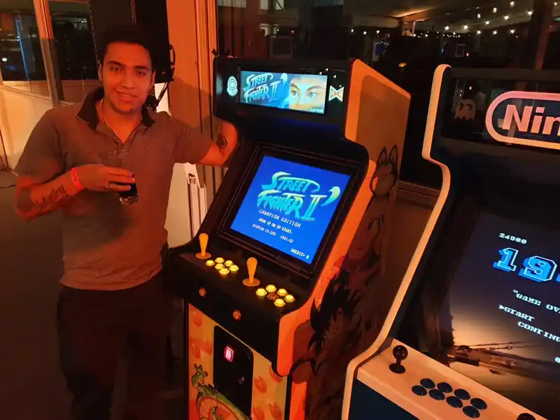 Participante junto a una máquina arcade temática de Street Fighter durante un evento nocturno con zona gaming interactiva y entretenimiento retro.