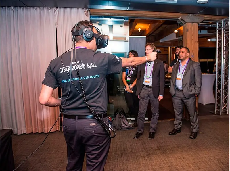 Participante utilizando unas gafas de realidad virtual y mandos de control durante una experiencia inmersiva en un evento corporativo. Mientras interactúa con el entorno virtual mediante movimientos físicos, varios asistentes observan la actividad con interés. La realidad virtual ofrece una experiencia innovadora y participativa que combina tecnología, entretenimiento y gamificación, ideal para congresos, ferias, team building y activaciones de marca.