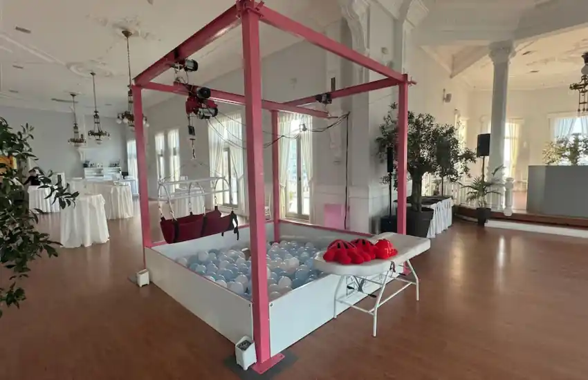 Atracción de Gancho Humano instalada en un elegante salón de eventos. La estructura incluye una piscina de bolas y un sistema de arnés suspendido que permite a los participantes vivir la experiencia de una máquina de garra a tamaño real. Ideal para eventos corporativos, ferias, congresos y celebraciones privadas.