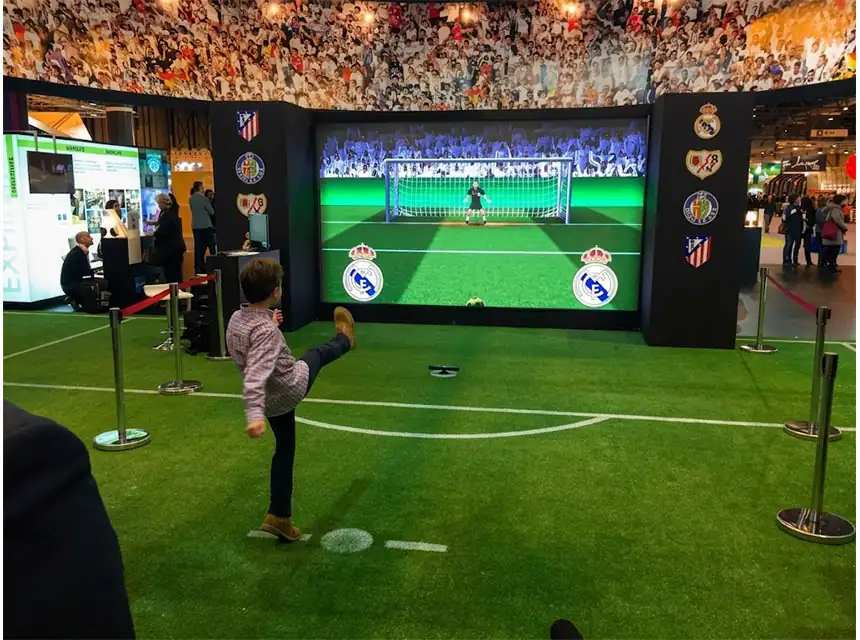 Nen xutant al simulador de futbol en un campus esportiu