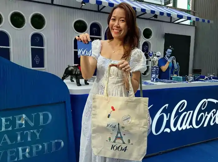 Mujer sonriente mostrando bolsa de tela personalizada en stand de activación de marca en evento
